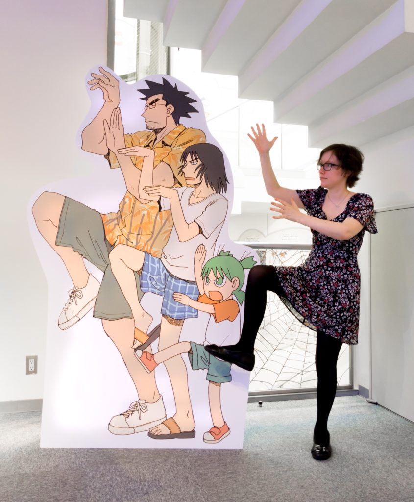A life sized cardboard cutout of three characters from the manga Yotsuba&! (Yotsuba, her father and Jumbo) strike kung fu poses. Next to them, with a look of great determination, I strike a matching pose.